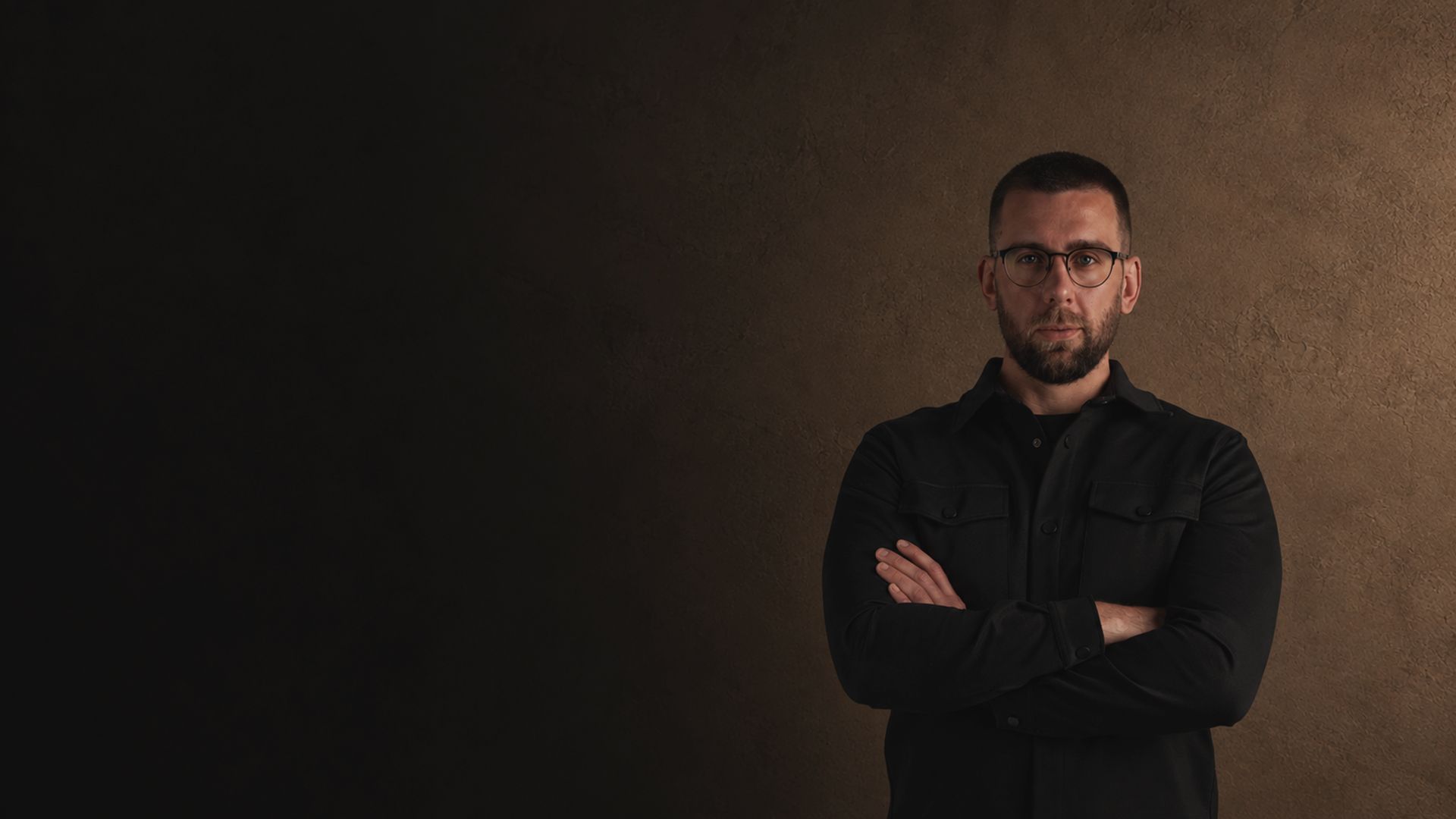 Stefan, brand identity designer behind MIST, arms crossed against a warm textured wall